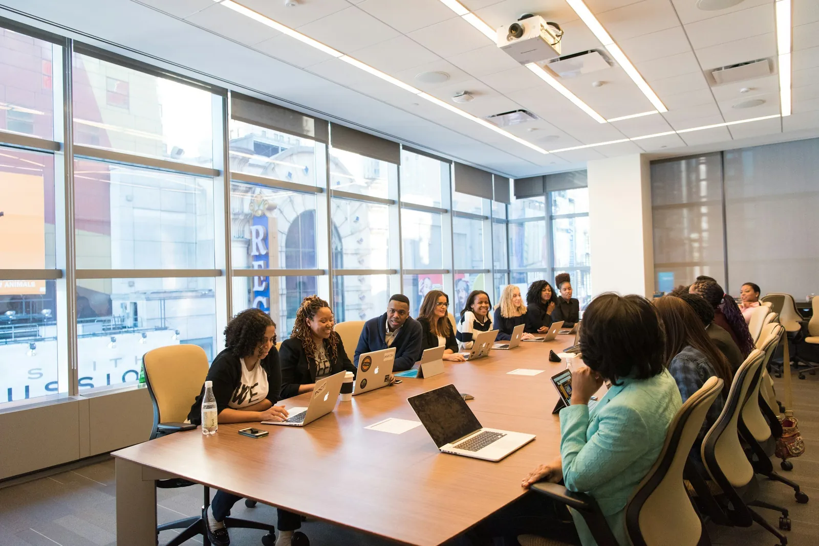 A meeting around a long boardroom table, with laptops open